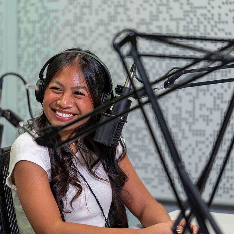 a student with headphones and mic in podcasting studio