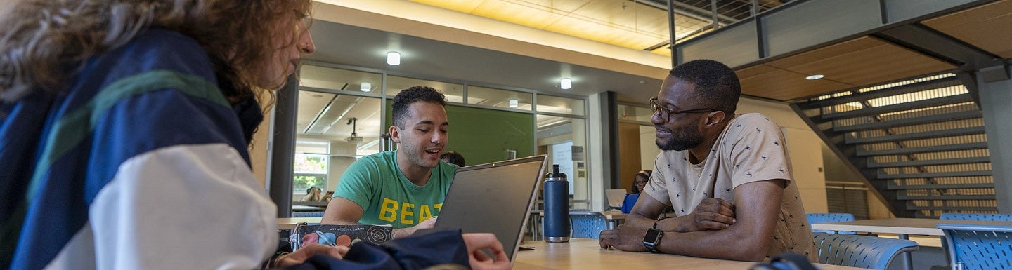 three people talking at a table, one person is using a laptop